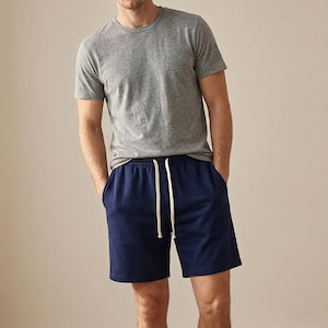 Può includere: Una maglietta grigia girocollo e pantaloncini blu navy con coulisse bianca. I pantaloncini hanno tasche. Abbigliamento casual.