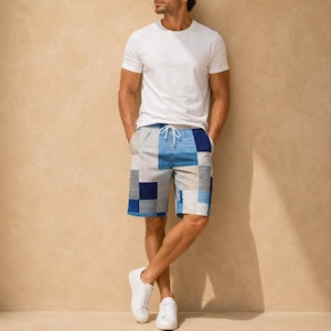 May include: A plain white short-sleeved crew neck t-shirt paired with knee-length shorts featuring a patchwork pattern of blue, light blue, gray, and white rectangular blocks, complete with a white drawstring waist and white sneakers.