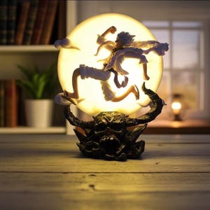 Puede incluir: Lámpara decorativa con un personaje saltando frente a una luna brillante. La figura lleva ropa blanca y beige, con una base detallada de color oscuro. La luna es de un amarillo suave y la lámpara está sobre una superficie de madera.