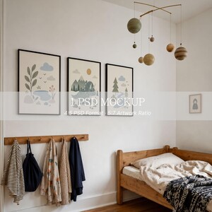 May include: Three framed wall art prints featuring nature and dinosaur illustrations in muted tones, hanging above a wooden coat rack with various garments and a wooden bed frame. A hanging mobile with spherical planet-like shapes is suspended above.