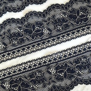 May include: A length of black lace trim featuring a floral pattern outlined in metallic silver thread. The lace has a scalloped edge and a decorative band of circular cutouts running horizontally through the center of the intricate design.
