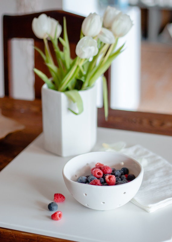 A hand-thrown white porcelain colander that doubles as a sculptural fruit bowl — 554 favorites proves people genuinely stop and want this thing.