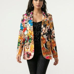 May include: A long-sleeve blazer featuring a vibrant, multi-coloured collage print with various graphic elements, including cartoon characters and text. The blazer is worn over a black top with white speckles, black slim-fit jeans, and black ankle boots.