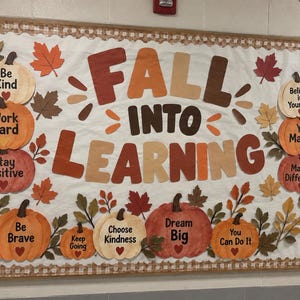 Op de afbeelding: Een prikbord met de tekst FALL INTO LEARNING in grote bruine en oranje letters. Het bord is versierd met papieren pompoenen en herfstbladeren in tinten rood, oranje en bruin, waarbij elke pompoen een positieve boodschap bevat.