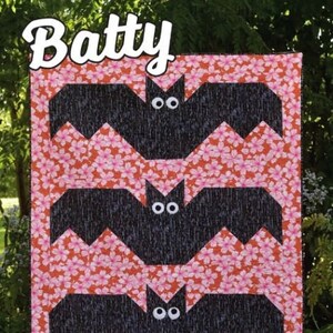 May include: A quilt pattern called "Batty" featuring three black bats with white eyes on a pink and orange floral background. The quilt pattern is by Running Doe Quilts for Villa Rosa Designs.