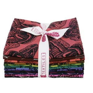 May include: A stack of folded fabric squares featuring a moth print in various colors including red, brown, orange, green, blue, purple, and black. The fabric bundle is tied with a white ribbon printed with the text ANNA MARIA TEXTILES.