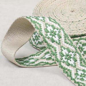 May include: A roll of beige and green woven ribbon with a geometric pattern. The ribbon is approximately 1 inch wide.