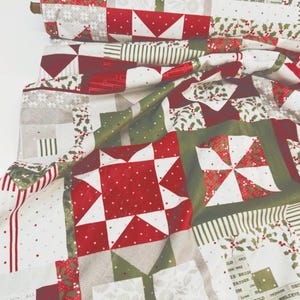 May include: A bolt of cotton fabric featuring a patchwork design with red, white, and green holiday patterns. The print includes star motifs, holly berries, striped sections, and text that reads "ALL IS BRIGHT" and "BELIEVE" in a repeating layout.