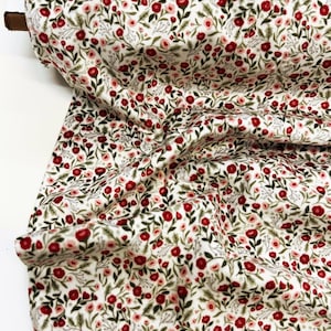 May include: A roll of fabric featuring a dense floral pattern on a white background. The design consists of small red and light pink flowers with green leaves and thin stems, creating a repetitive botanical print across the entire textile surface.