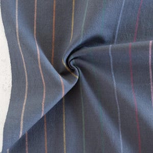 May include: Close-up of a dark blue fabric with vertical stripes in various colors, including orange, yellow, green, and pink. The fabric is folded and twisted, showing its texture and the interplay of colors.