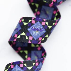 May include: A length of woven ribbon featuring a repeating geometric pattern of black, pink, and lime green squares. The design includes blue diamond-shaped motifs, each containing a stylized purple dragonfly illustration with radiating light lines.