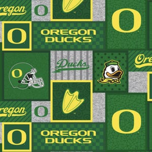 May include: A fabric pattern featuring the Oregon Ducks logo, text, and imagery in green, yellow, and grey. The design includes football helmets, duck feet, the letter O, and the words Oregon Ducks in various block and script fonts.