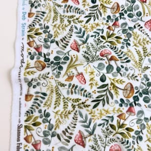May include: White fabric with a watercolor design featuring mushrooms and foliage in shades of green, brown, and red. The fabric has a repeating pattern of various leaves and fungi. The text "Effie's Woods by Deb Strain" is printed on the side.
