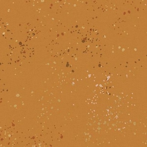 May include: A close-up of a fabric with a textured surface. The fabric is a warm orange-brown color, with small, irregular spots of white, brown, and tan scattered across the surface.