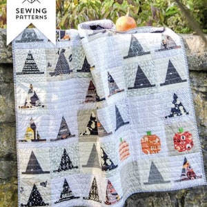 May include: A white quilt with a black and white pattern of witch hats and pumpkins. The quilt is hanging on a stone wall. The text "Halloween Haberdashery" is at the bottom of the image.