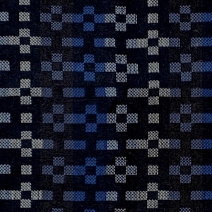 May include: A woven textile fabric featuring a repeating geometric pattern of small squares and rectangles in shades of dark navy blue, medium blue, and light gray, creating a structured grid-like design across the entire surface of the material.