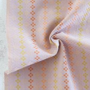 May include: Close-up of a woven fabric with a repeating pattern of vertical stripes. The fabric features a pastel color palette of pink, yellow, and orange. The fabric is slightly crumpled, showing the texture and weave of the material.