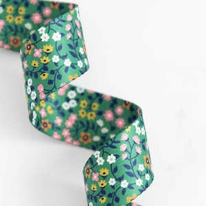 May include: Green floral ribbon with a repeating pattern of small pink, yellow, and white flowers and blue vines. The ribbon is curled and displayed against a white background. This decorative ribbon is suitable for crafts and gift wrapping.