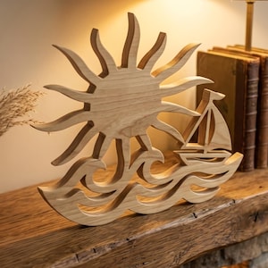 May include: Wooden decorative piece with a nautical theme, depicting a sun, sailboat, and waves. The sun has pointed rays, and the sailboat has a triangular sail. The waves are carved at the base. The wood has a natural, light brown colour.