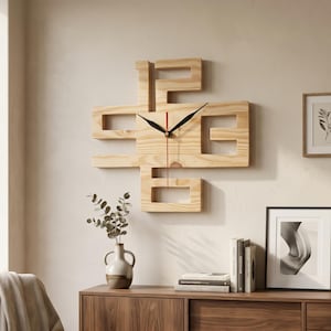 May include: A contemporary wooden wall clock with a distinctive geometric shape. The clock has a natural wood finish, black hands, and a red second hand. It's mounted on a light wall, with decorative items in the background. The clock measures approximately 40 cm across.