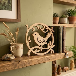 Peut inclure: Décoration en bois représentant un oiseau dans un cadre circulaire avec des feuilles. La couleur naturelle du bois contraste avec le mur vert et l'étagère en bois. L'oiseau est perché sur une branche.