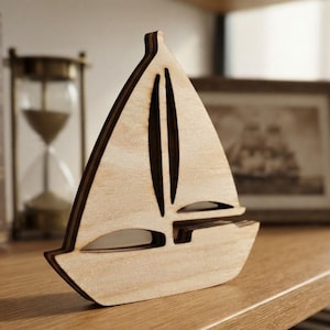 May include: A light-colored wooden sailboat cutout featuring a layered design with dark-toned edges. The sailboat has a triangular sail shape and a horizontal hull section, showcasing a clean, flat surface with visible wood grain texture throughout.