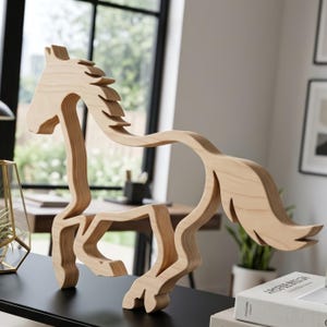 Pode incluir: Escultura de cavalo em madeira com crina e cauda fluídas. A madeira de cor clara é cortada em uma forma estilizada, com detalhes em camadas que criam profundidade. O cavalo está em uma postura de corrida, adequado para decoração de casa.