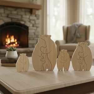Puede incluir: Un conjunto de cuatro rompecabezas de madera de una familia de osos. Cada figura de oso marrón claro está diseñada para entrelazarse, representando a un padre y un hijo abrazándose. Las piezas se exhiben sobre una mesa de madera clara.