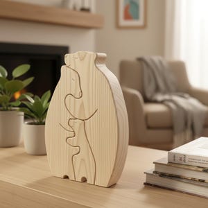 Może przedstawiać: Jasna drewniana rzeźba przedstawiająca rodzinę niedźwiedzi, z dużym niedźwiedziem obejmującym mniejszego niedźwiedzia i maleńkim niedźwiedziem pośrodku. Rzeźba stoi na jasnym drewnianym stole, z roślinami i książkami w tle.