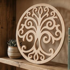 Puede incluir: Una pieza de arte mural circular de madera clara con un diseño de árbol cortado a láser que presenta ramas y raíces con volutas intrincadas. La placa de madera tiene un acabado natural liso y se exhibe sobre un estante de madera.