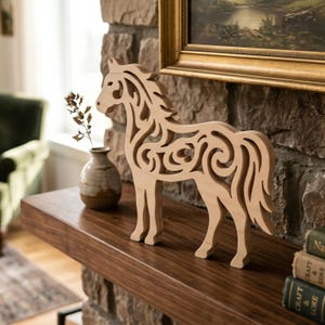 Peut inclure: Une figurine de cheval en bois avec des motifs découpés complexes se dresse sur une surface en bois foncé. Le cheval de couleur claire a une crinière et une queue fluides, et est exposé sur une cheminée avec un vase et une œuvre d'art encadrée.