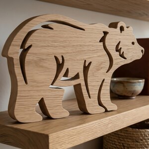 Könnte beinhalten: Eine hellbraune Holzfigur in Form eines Bären mit einem ausgeschnittenen Design. Der Bär steht auf einem Holzregal. Die Silhouette des Bären ist sichtbar, mit Aussparungen für Beine, Körper und Kopf. Die Figur ist ein dekoratives Element.