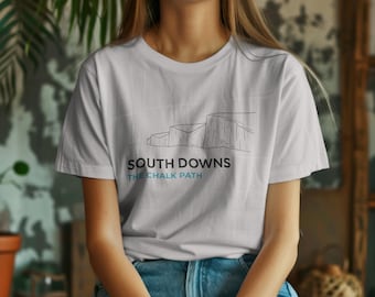 May include: A light gray t-shirt featuring a black and blue graphic of a coastal landscape. The text "SOUTH DOWNS" is above "THE CHALK PATH" in a sans-serif font. The shirt is made of a soft material and is suitable for casual wear.