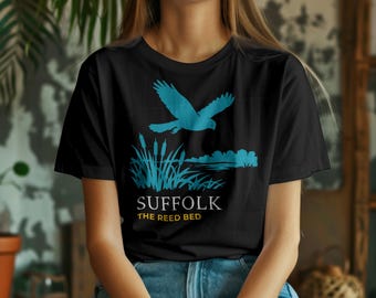 May include: Black t-shirt with a teal graphic of a bird flying over reeds and water. The text "SUFFOLK THE REED BED" is printed below the graphic. The shirt is made of a soft material.