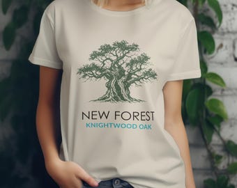 May include: A light beige t-shirt featuring a detailed green illustration of a large tree. Below the tree is the text "NEW FOREST" in black and "KNIGHTWOOD OAK" in teal. The shirt is short-sleeved and has a crew neck.