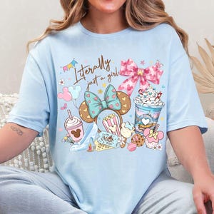 K&ouml;nnte beinhalten: Hellblaues T-Shirt mit einer skurrilen Grafik. Das Design umfasst ein Minnie Mouse Ohren-Stirnband, Popcorn, einen High Heel und ein Getr&auml;nk. Der Text "Literally just a girl" ist ebenfalls enthalten.