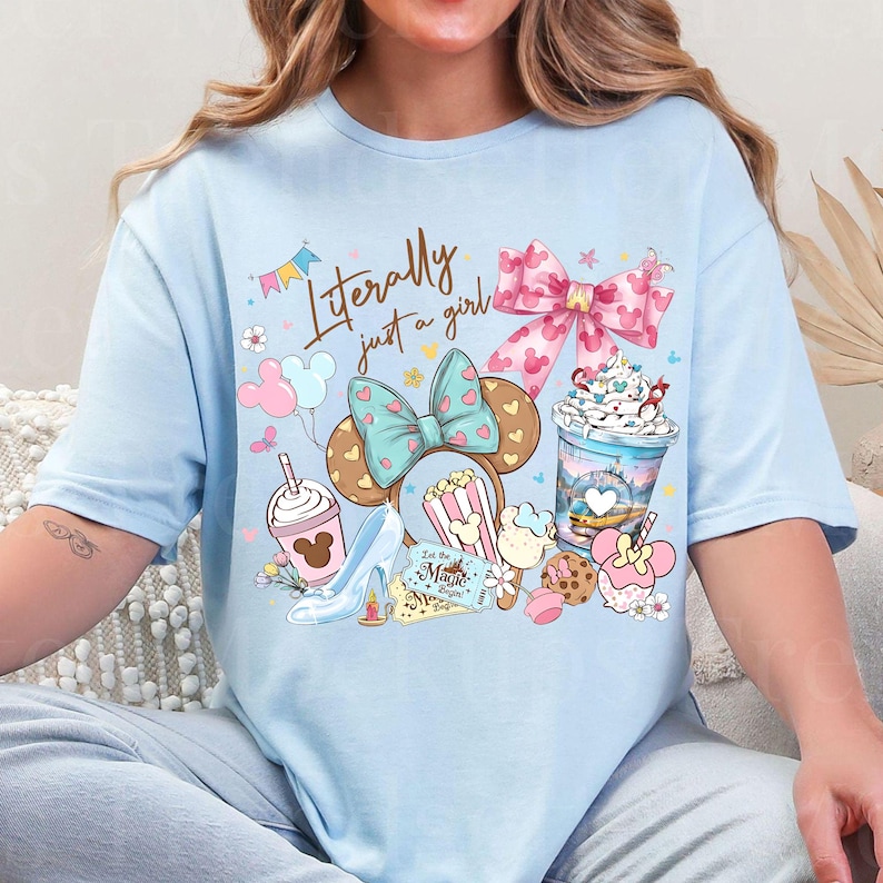 K&ouml;nnte beinhalten: Hellblaues T-Shirt mit einer skurrilen Grafik. Das Design umfasst ein Minnie Mouse Ohren-Stirnband, Popcorn, einen High Heel und ein Getr&auml;nk. Der Text "Literally just a girl" ist ebenfalls enthalten.