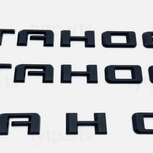 Puede incluir: Letras de emblema "TAHOE" de plástico negro. Se muestran tres conjuntos de la palabra "TAHOE", cada uno en una fuente en negrita sin serifa. Las letras están espaciadas uniformemente y parecen ser piezas individuales.