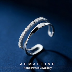 May include: A silver-colored ring with a double-band design. One band is adorned with small, clear gemstones, while the other is smooth and polished. The ring is set against a dark blue background. The text "AHMADFIND Handcrafted Jewellery" is at the bottom.