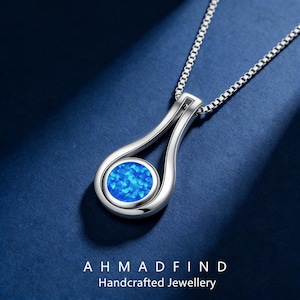 May include: A silver pendant necklace with a teardrop design. The pendant features a round, vibrant blue opal stone. The necklace is displayed on a dark blue surface. The text "AHMADFIND Handcrafted Jewellery" is at the bottom.