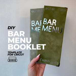 Op de afbeelding: Twee hoge, rechthoekige barmenu-boekjes met een zachte, suède-achtige textuur in olijfgroen. Het voorste boekje heeft zilverkleurige folietekst met BAR MENU, OCT 02, 2026 en THE LUNDQUISTS. Het tweede boekje erachter toont vergelijkbare zilveren tekst.