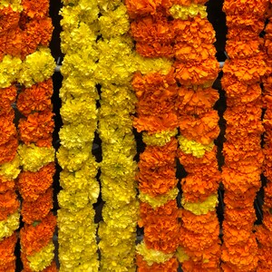 May include: A series of vertical floral garlands composed of densely packed marigold blossoms. The strands alternate between vibrant orange and bright yellow petals, creating a textured, layered appearance across the entire display.