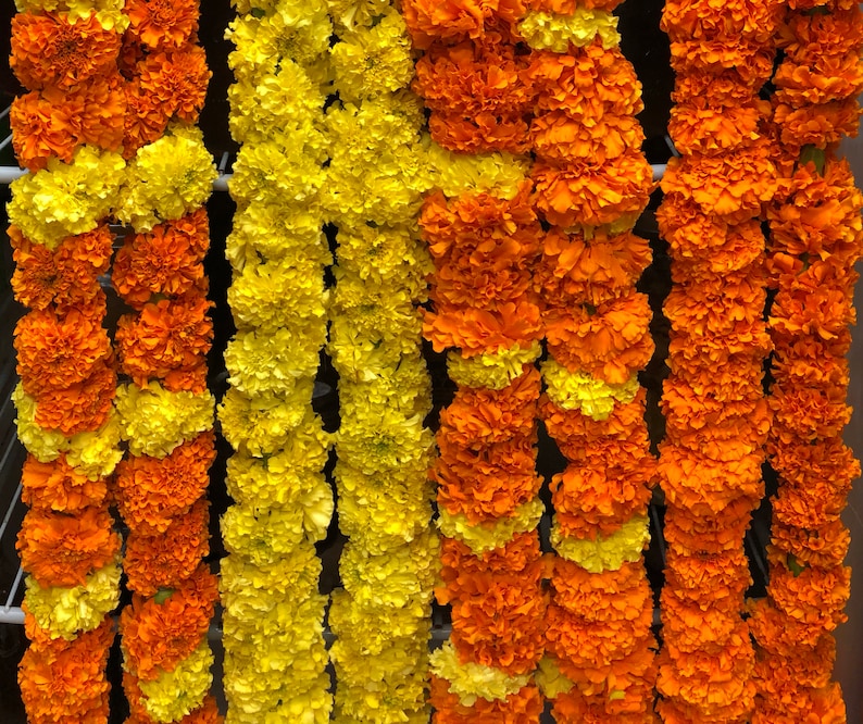 May include: A series of vertical floral garlands composed of densely packed marigold blossoms. The strands alternate between vibrant orange and bright yellow petals, creating a textured, layered appearance across the entire display.