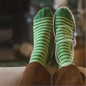 A pair of feet wearing green and white striped socks, with a drawing of a shoe on the right foot.