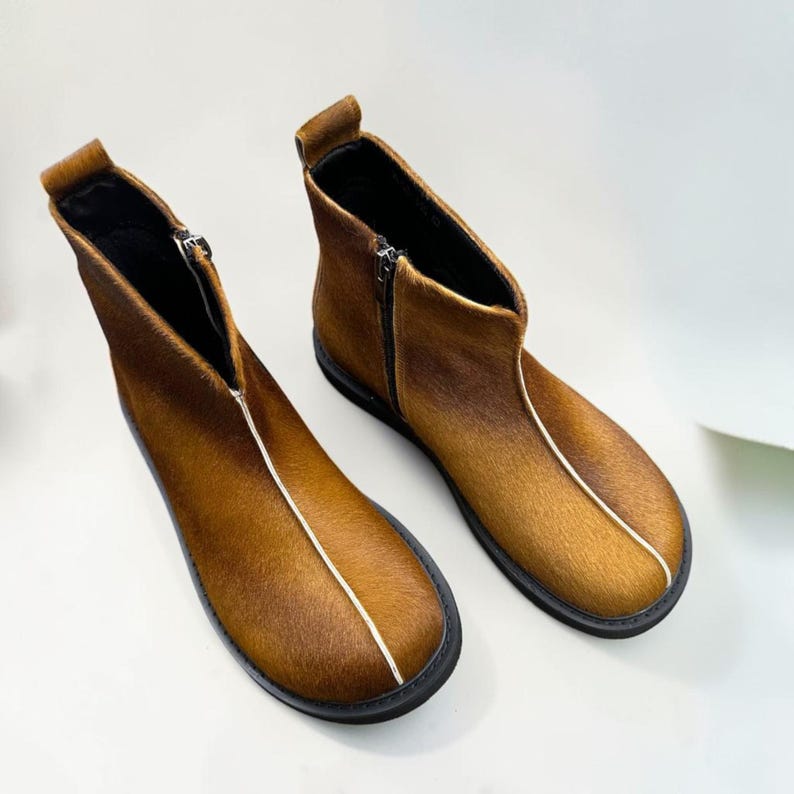 A pair of brown leather boots with black soles and zippers, placed on a white background.