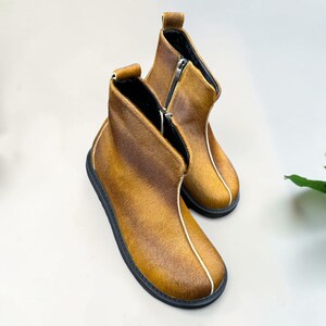 A pair of brown leather boots with black soles and zippers, placed on a white background.