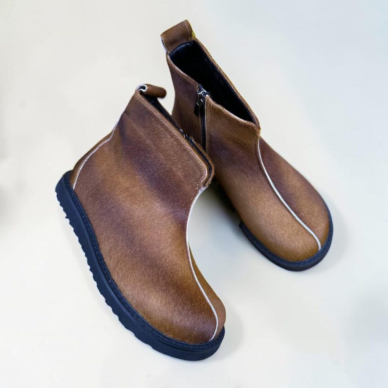 A pair of brown leather boots with black soles and zippers, placed on a white background.