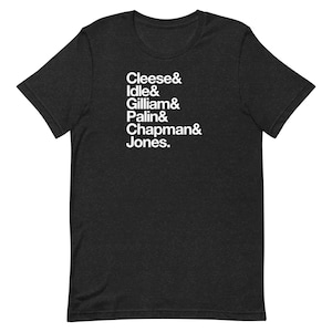May include: Charcoal grey t-shirt featuring white text listing the names "Cleese & Idle & Gilliam & Palin & Chapman & Jones." The shirt is made of a soft material and has short sleeves.