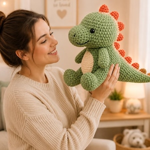 May include: A crocheted dinosaur plush toy featuring a sage green body, a cream-colored belly, and a row of small orange spikes running along its back and tail. The toy has black safety eyes and a stitched mouth, crafted with a textured yarn finish.