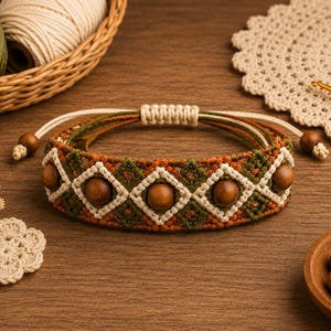 Op de afbeelding: Een macramé armband met een geweven patroon van olijfgroen, roestoranje en crèmekleurig koord. Het ontwerp bevat gladde, ronde, donkerbruine houten kralen gecentreerd in ruitvormige crèmekleurige koordframes met een verstelbare schuifknoopsluiting.